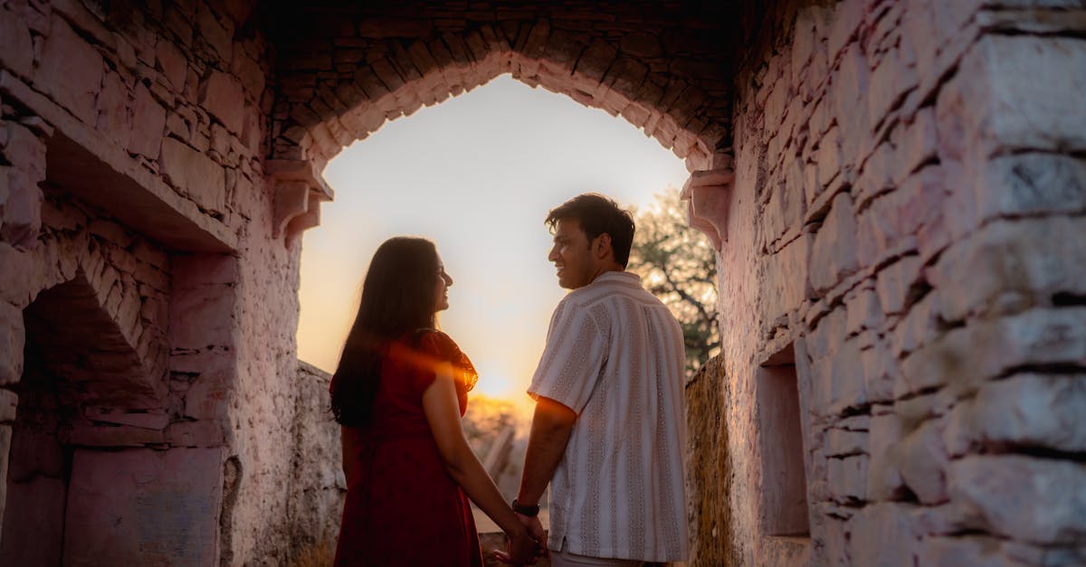A romantic couple holds hands under an ancient archway at sunset, exuding peaceful love and connection.